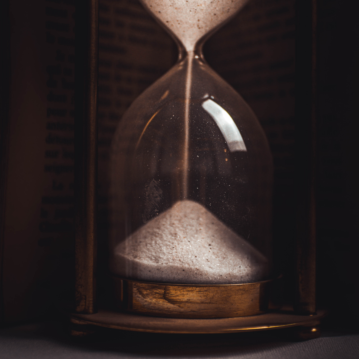 Antique hourglass with sand falling against a dark background.